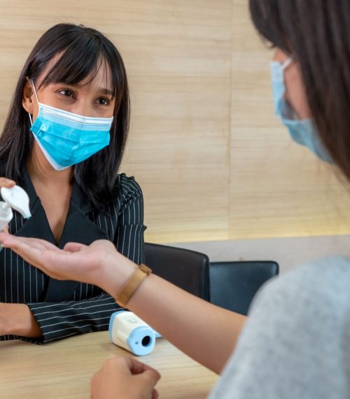 receptionist-and-guest-wearing-face-mask-at-front-desk-while-having-conversation-in-office-or-hospital